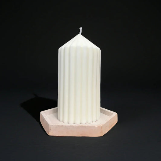 Weiße handgemachte Kerze mit Rillenstruktur auf sechseckigem Untersetzer vor dunklem Hintergrund