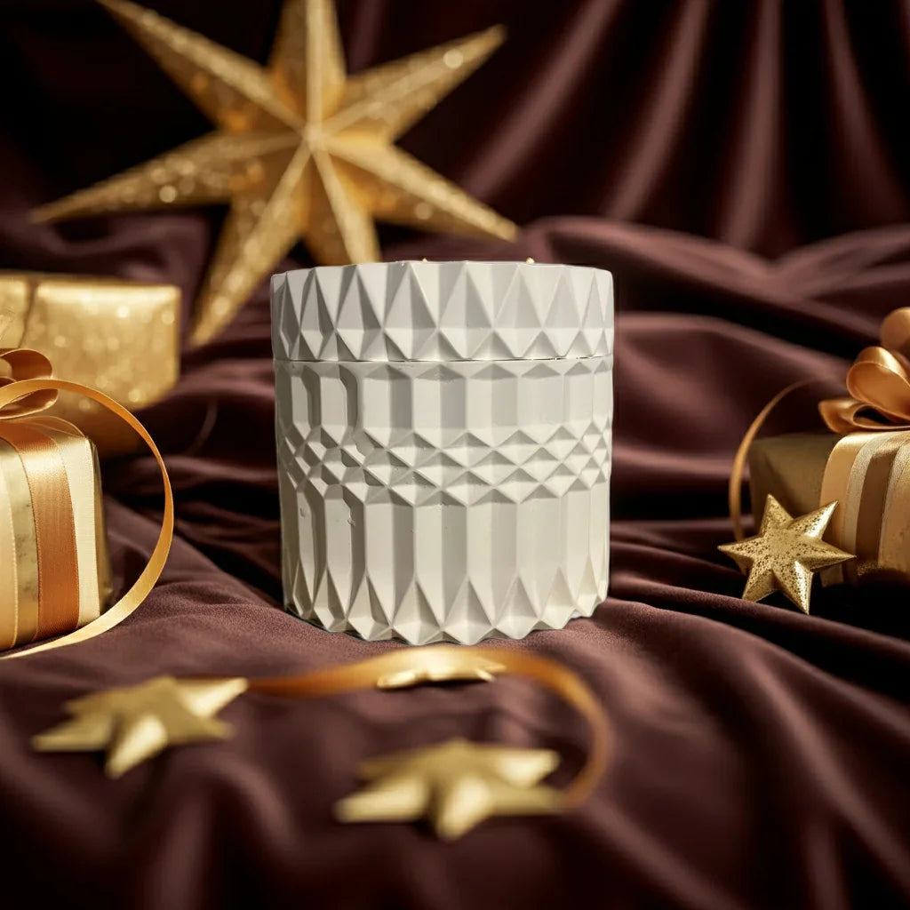 Handgemachte Kerze im weißen, geometrischen Glas, dekoriert mit goldenen Sternen und Geschenken