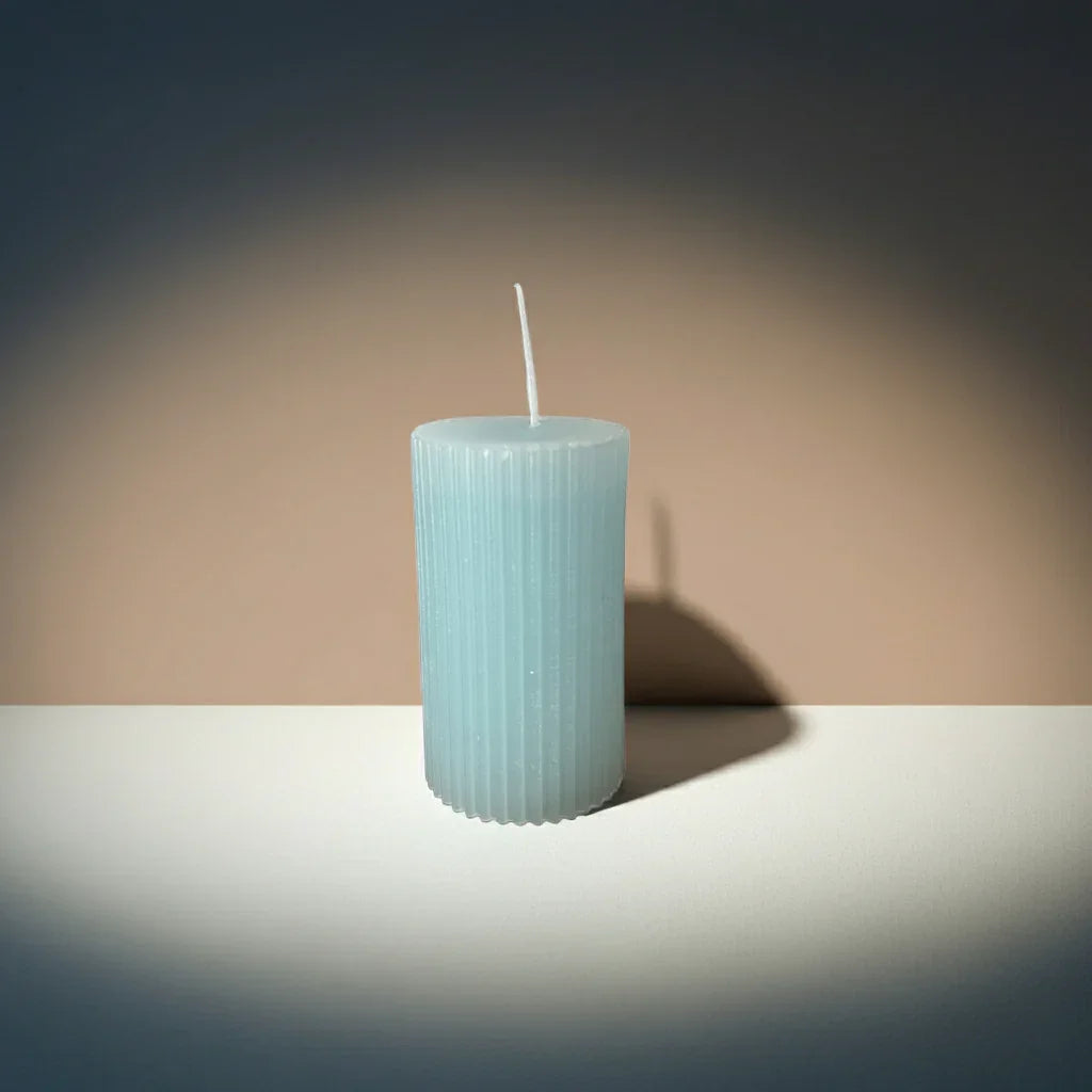 Handgemachte, zylindrische Stumpenkerze in Hellblau mit geriffelter Oberfläche auf Tisch