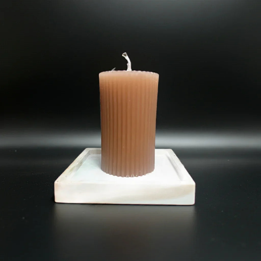 Braune, handgemachte Kerze mit Rillenstruktur auf quadratischer Unterlage vor schwarzem Hintergrund