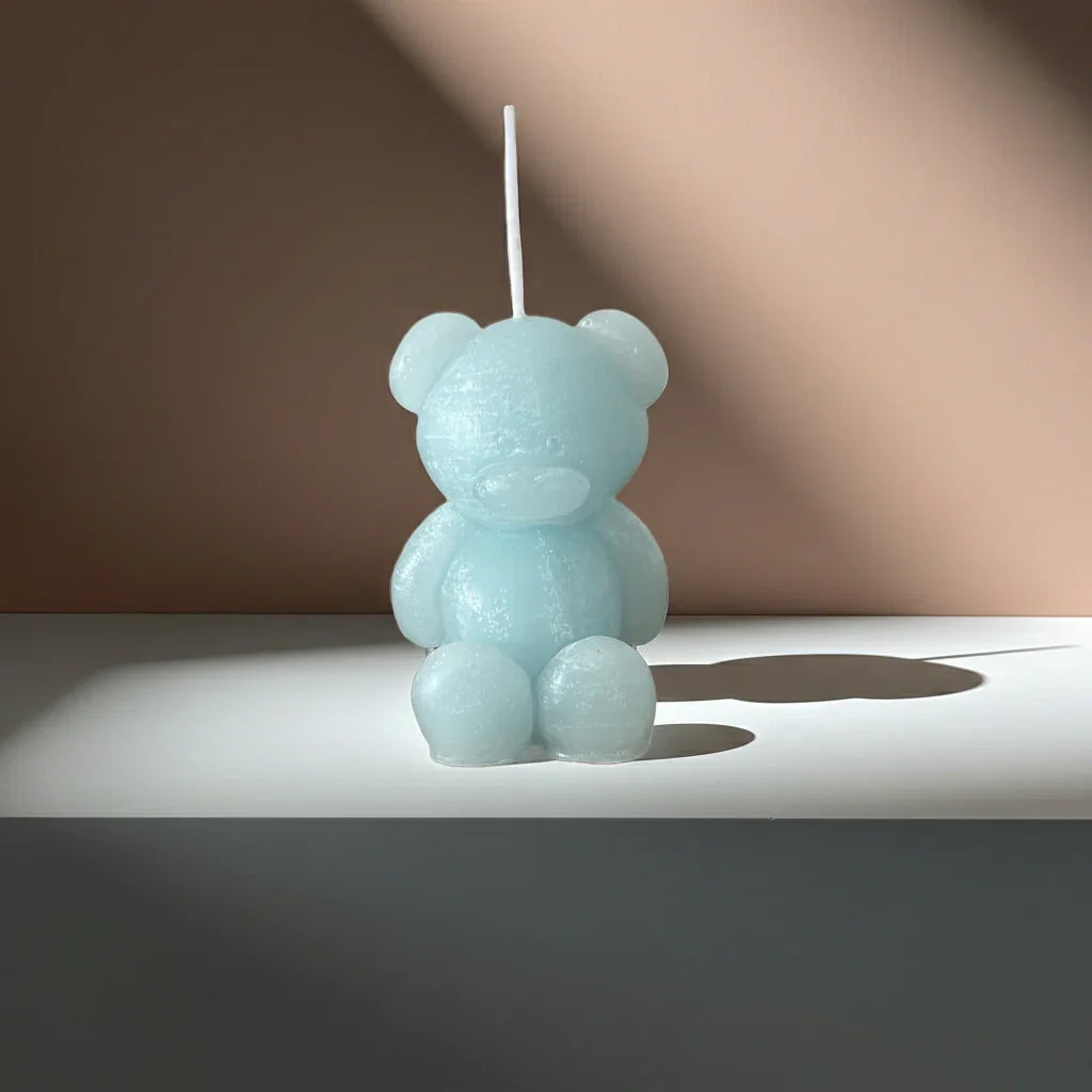 Handgemachte Kerze in Bärenform, hellblau, auf weißem Tisch im sanften Licht