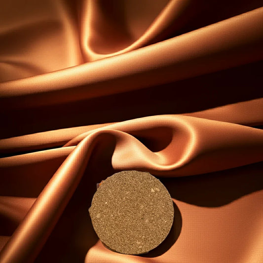 Handgemachte, runde Naturkerze auf elegant drapiertem, glänzendem Stoff in Braun.