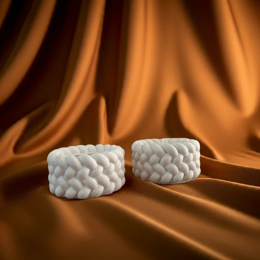 Zwei handgemachte, weiße Kerzen mit geflochtenem Muster auf orangefarbenem Stoff