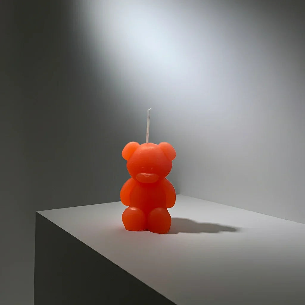 Handgemachte Kerze in Bärenform, orange, auf hellem Podest, stimmungsvolles Licht