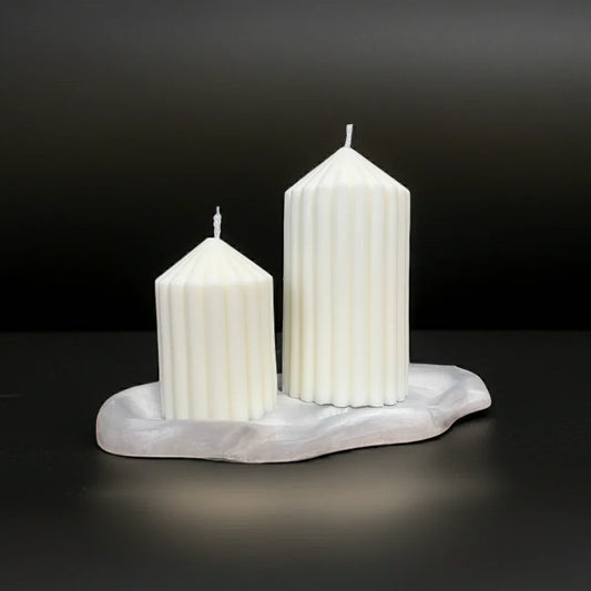 Zwei handgemachte Stumpenkerzen mit Rillenmuster auf grauer Ablage, schwarzer Hintergrund