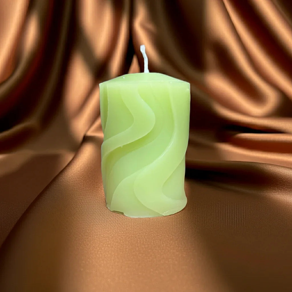 Handgemachte grüne Kerze mit welligem Muster auf braunem Stoff, stimmungsvolles Licht