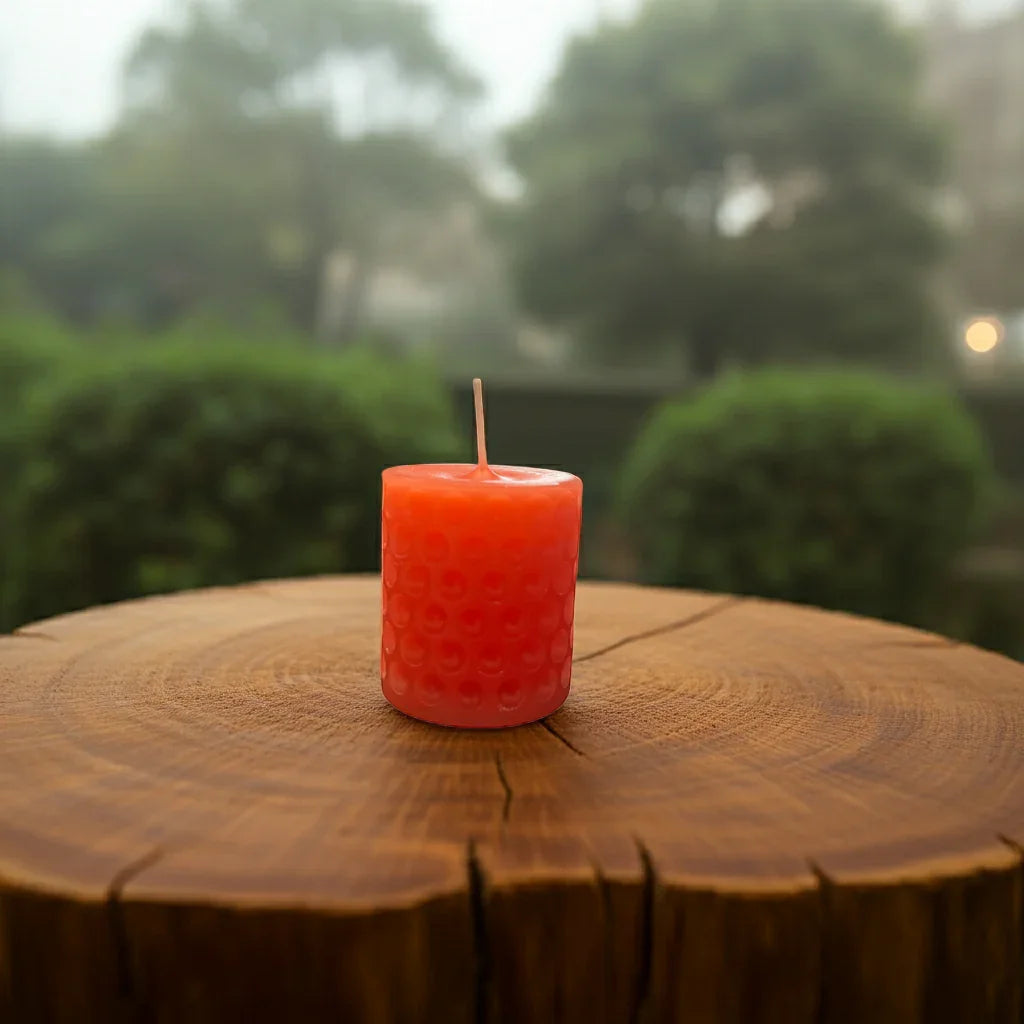 Handgemachte orange Stumpenkerze mit Wabenstruktur auf Holz, Natur im Hintergrund