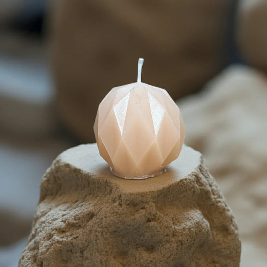 Handgemachte Kerze in Diamantform, beige, auf sandigem Stein, dekorative Geschenkidee