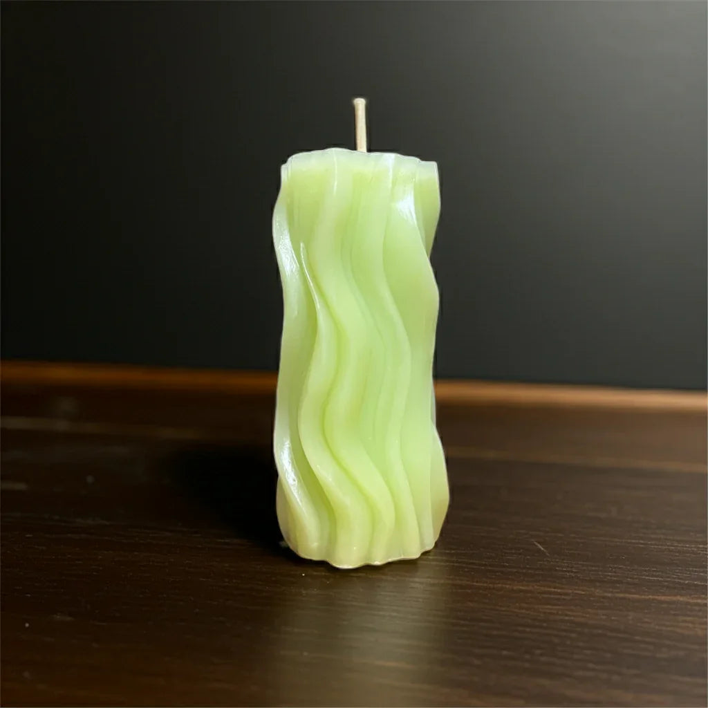 Wellige, handgemachte grüne Kerze auf dunklem Holztisch, dekorative Wohnkerze