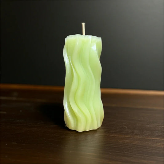 Wellige, handgemachte grüne Kerze auf dunklem Holztisch, dekorative Wohnkerze