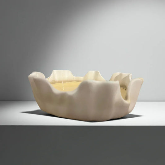 Handgemachte Kerze in organisch geformtem, weißen Gefäß auf neutralem Hintergrund