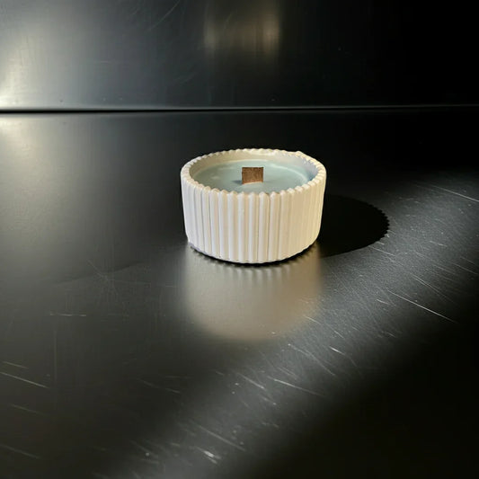 Handgemachte Kerze im weißen geriffelten Becher mit Holzdocht auf dunkler Oberfläche