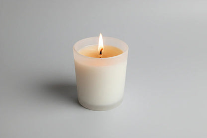 Handgemachte Duftkerze im Glas, brennend, auf hellem Hintergrund, minimalistisch